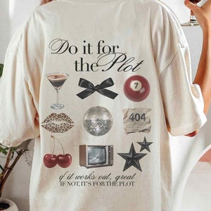 May include: A white oversized t-shirt with the text "Do it for the Plot" and various graphic elements, including a martini glass, a bow, a billiard ball, a disco ball, a 404 error sign, cherries, a television, and stars. The shirt is shown on a model wearing it.