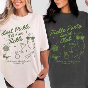 May include: Two t-shirts with a pickle theme. One is ivory with green text that says "Last Pickle I'll Ever Tickle" and the other is dark gray with green text that says "Pickle Party Social Club". Both shirts have a pickle, a martini glass, a ring, and a bottle of champagne graphic.