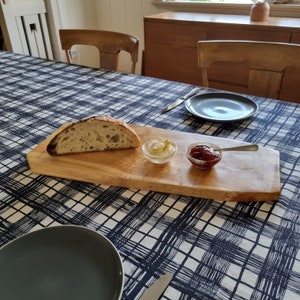 May include: A wooden serving board with a slice of sourdough bread, a small bowl of butter, and a small bowl of red jam. The board is on a black and white checkered tablecloth.