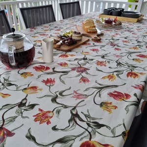 May include: A white tablecloth with a floral pattern of red and yellow tulips. The tablecloth is laid out on a table with a pitcher of tea, a glass of milk, and a plate of food.