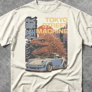 May include: Ivory t-shirt with a graphic design featuring Japanese text, a car, and a dragon-like creature. The text "TOKYO STREET MACHINE" is also visible. The shirt is described as being made with "Comfort colors."