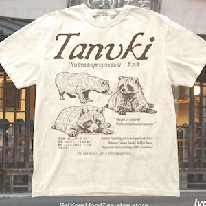 Vintage tanuki t-shirt featuring Japanese raccoon dog illustrations in a field guide style layout, printed on ivory Comfort Colors tee with retro nature aesthetic and detailed wildlife graphics