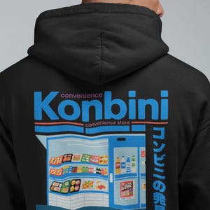 May include: Black hoodie with a graphic of a convenience store, the word "Konbini" in blue, and Japanese text. The design includes the phrase "Where hunger meets adventure" in white text at the bottom.