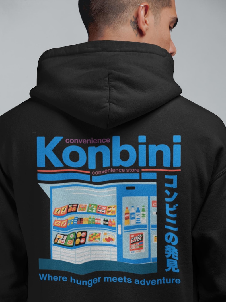 May include: Black hoodie with a graphic of a convenience store, the word "Konbini" in blue, and Japanese text. The design includes the phrase "Where hunger meets adventure" in white text at the bottom.
