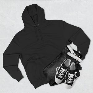 May include: A black hooded sweatshirt with a drawstring, paired with dark denim jeans, a white belt, and black and white sneakers. The casual outfit is laid out on a white surface.