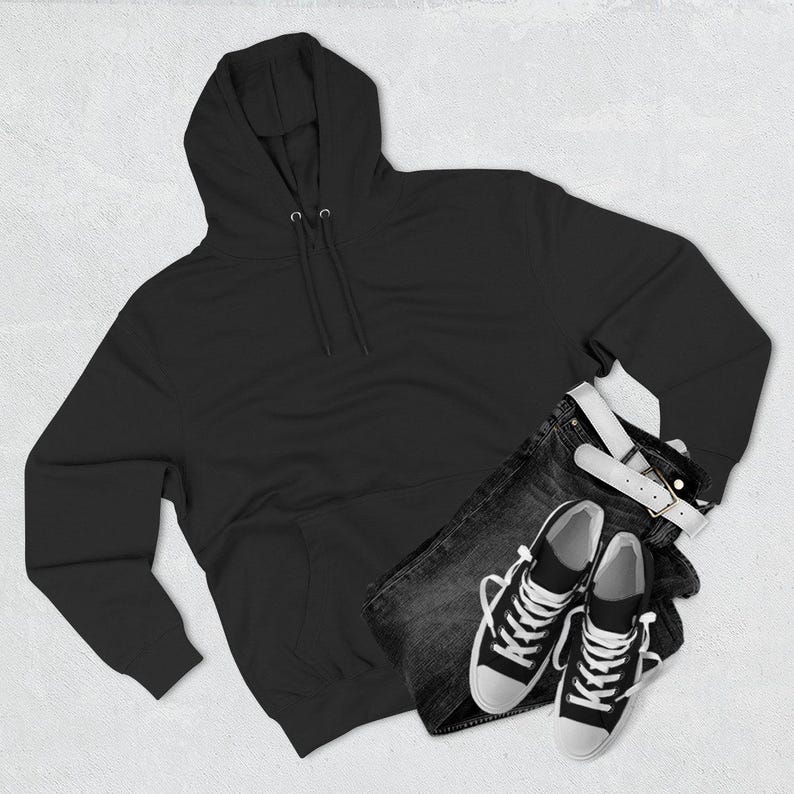 May include: A black hooded sweatshirt with a drawstring, paired with dark denim jeans, a white belt, and black and white sneakers. The casual outfit is laid out on a white surface.