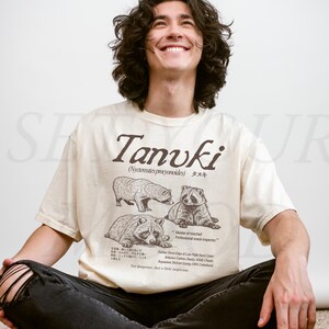 man wearing ivory tanuki t-shirt with japanese raccoon dog illustration, vintage wildlife graphic printed on comfort colors shirt, clean studio background