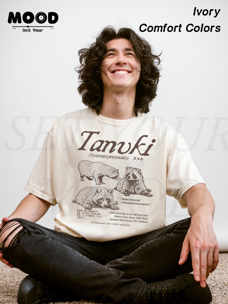 man wearing ivory tanuki t-shirt with japanese raccoon dog illustration, vintage wildlife graphic printed on comfort colors shirt, clean studio background