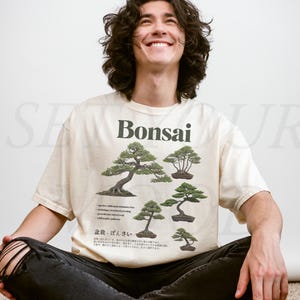 May include: Ivory-colored t-shirt with a Bonsai tree graphic. The shirt features several illustrations of Bonsai trees, along with text in English and Japanese. The shirt also has the text "Comfort Colors" and the word "Ivory" printed on it.