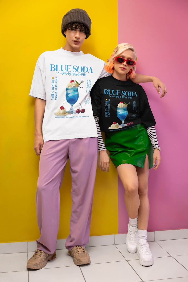 May include: Two people wearing t-shirts with a blue soda graphic. The white shirt has a blue soda design with Japanese text. The black shirt has the same design. The background is yellow and pink.