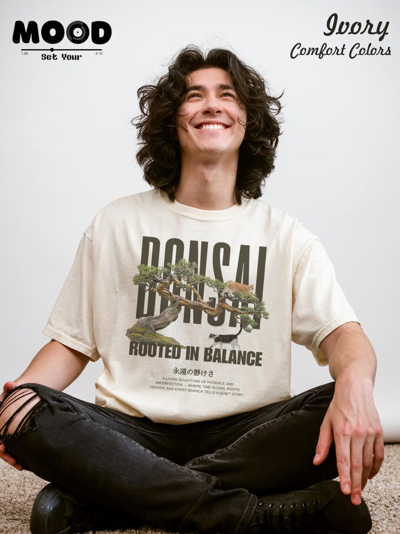 May include: Ivory-colored t-shirt with a bonsai tree graphic and the text "BONSAI ROOTED IN BALANCE." The shirt also features Japanese text and the words "Ivory Comfort Colors." The person is wearing black jeans.