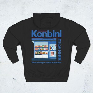 May include: Black hoodie featuring a graphic of a convenience store with the word "Konbini" in blue and Japanese text. The phrase "Where hunger meets adventure" is printed below the store illustration.