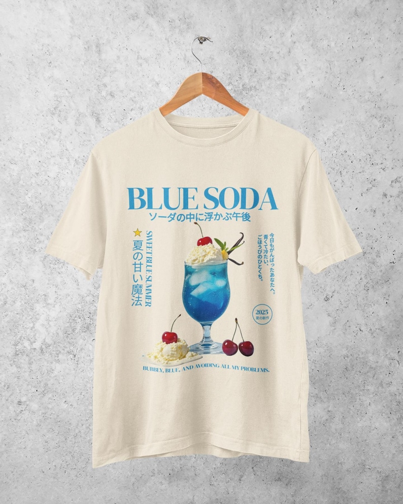 May include: Cream-colored t-shirt with a blue graphic of a blue soda drink with cherries and whipped cream. Text includes "BLUE SODA" and Japanese characters. The phrase "Bubbly, blue, and avoiding all my problems" is also present.