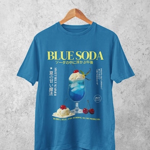 May include: Blue t-shirt with a graphic of a blue soda drink with whipped cream and cherries. The text "BLUE SODA" and Japanese characters are printed in yellow. The phrase "BUBBLY, BLUE, AND AVOIDING ALL MY PROBLEMS" is printed at the bottom.