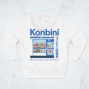 May include: White hoodie featuring a graphic of a convenience store with the word "Konbini" in blue and Japanese text. The design includes the phrase "Where hunger meets adventure."