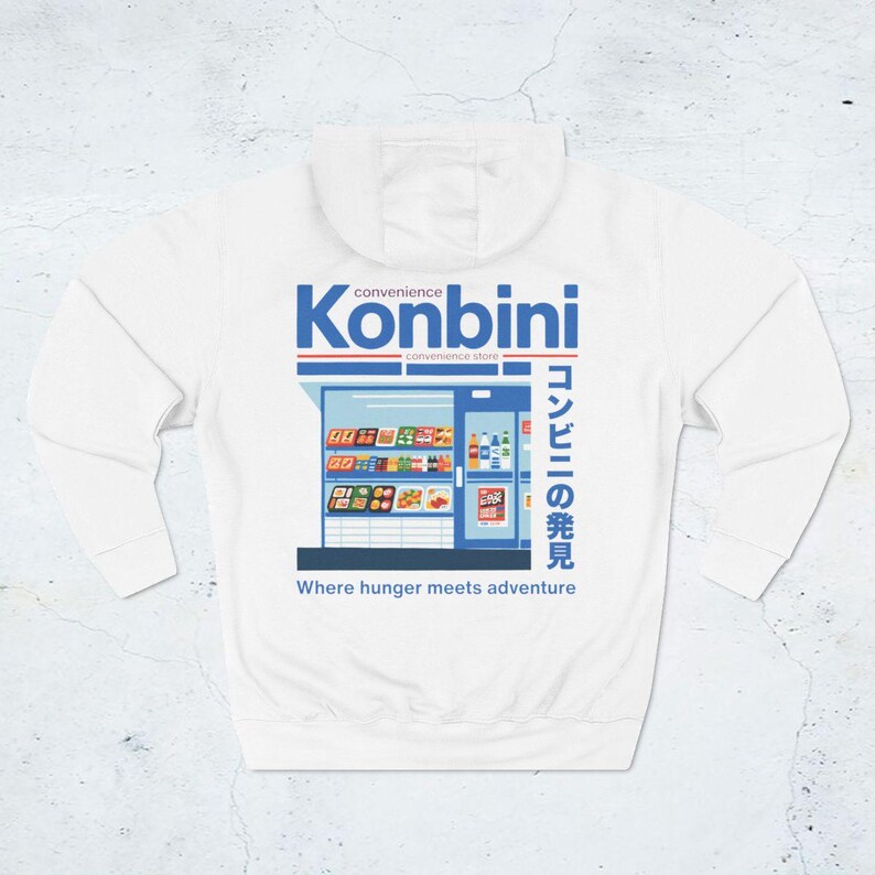 May include: White hoodie featuring a graphic of a convenience store with the word "Konbini" in blue and Japanese text. The design includes the phrase "Where hunger meets adventure."