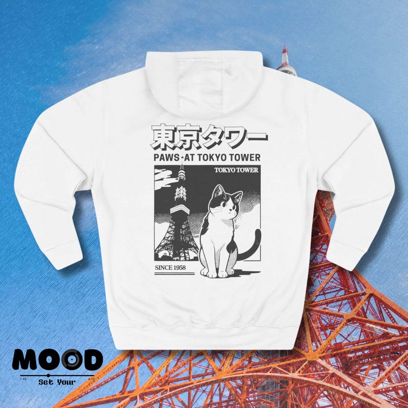 May include: White hoodie with a graphic of a black and white cat and the Tokyo Tower. Text includes "Paws at Tokyo Tower" and "Since 1958". The word "MOOD" is printed at the bottom. The hoodie has a hood and long sleeves.