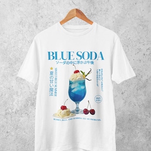 May include: White t-shirt with a blue graphic that says "BLUE SODA" in large letters. The graphic includes a blue drink with whipped cream, cherries, and text in Japanese. The text "SWEET BLUE SUMMER" is also present.