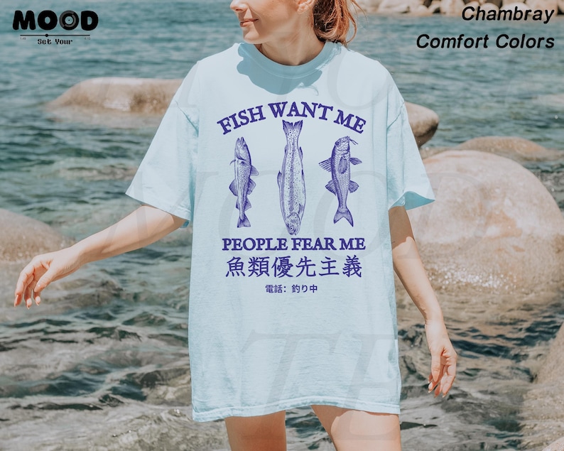 May include: Light blue t-shirt with the text "FISH WANT ME PEOPLE FEAR ME" and Japanese text. The shirt features three fish illustrations in a dark blue color. The shirt is made of a soft, comfortable material.