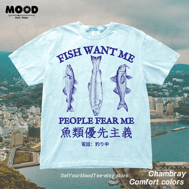 Light blue Comfort Colors t-shirt featuring “Fish Want Me People Fear Me” slogan with three vintage-style fish illustrations and Japanese text, retro fishing graphic tee for anglers.