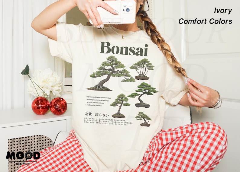 May include: Ivory-colored t-shirt with a Bonsai tree graphic. The shirt features multiple illustrations of bonsai trees and Japanese text. The words "Ivory" and "Comfort Colors" are printed on the top right of the shirt.