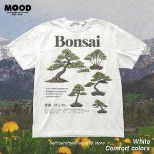May include: White t-shirt featuring a Bonsai design. The shirt displays several illustrations of Bonsai trees, with the word "Bonsai" in a dark green font. Additional text includes botanical details and Japanese characters. The shirt is labeled "Comfort colors".