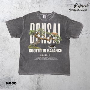 May include: Dark grey t-shirt with a bonsai tree graphic and the word "BONSAI" in large white letters. The design includes two cats and the text "ROOTED IN BALANCE". Additional text at the bottom describes the bonsai.