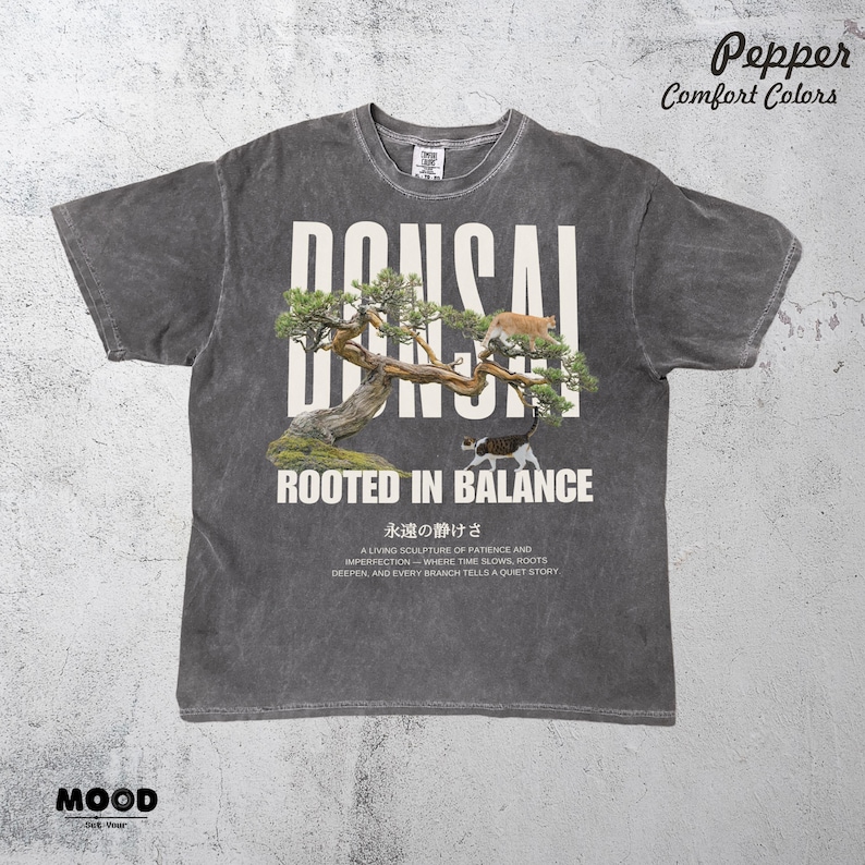 May include: Dark grey t-shirt with a bonsai tree graphic and the word "BONSAI" in large white letters. The design includes two cats and the text "ROOTED IN BALANCE". Additional text at the bottom describes the bonsai.