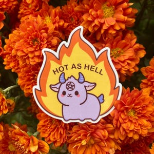 Może przedstawiać: Naklejka z kreskówkową kozą z rogami i pentagramem na czole. Koza jest fioletowa i otoczona płomieniami. Tekst "HOT AS HELL" jest napisany nad kozą.