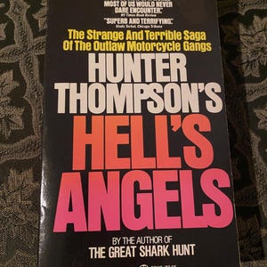 May include: A paperback book titled "Hunter Thompson's Hell's Angels" with a black cover and bold, colorful lettering. The title is in large, pink and orange letters. The book also features quotes and the author's name.