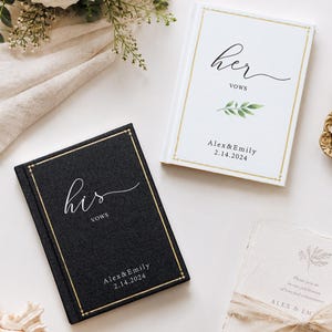 May include: Two hardcover vow books, one black and one white, featuring gold foil borders and text. The black book reads 'his vows' and the white book reads 'her vows', both personalised with 'Alex & Emily' and the date '2.14.2024' in black ink.