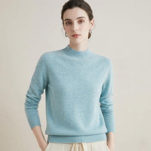 Könnte beinhalten: Hellblauer Pullover mit Stehkragen. Der langärmlige Pullover ist aus einem weichen Material gefertigt und hat gerippte Bündchen und Saum. Das Model trägt den Pullover mit hellen Hosen.
