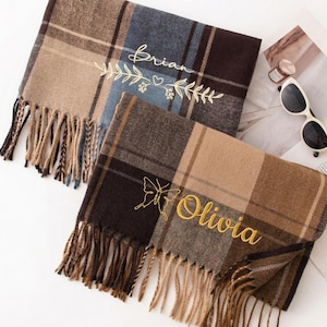 May include: Two plaid scarves with fringe, one in brown and blue, the other in brown and tan. The brown and blue scarf has the name "Brian" embroidered in gold. The brown and tan scarf has the name "Olivia" embroidered in gold.