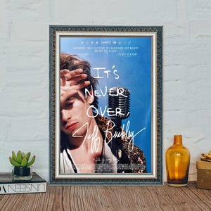 Może przedstawiać: Oprawiony plakat z niebieskim tłem, z napisem "It's Never Over, Jeff Buckley". Obraz zawiera zabytkowy mikrofon i portret osoby. Rama jest srebrna.