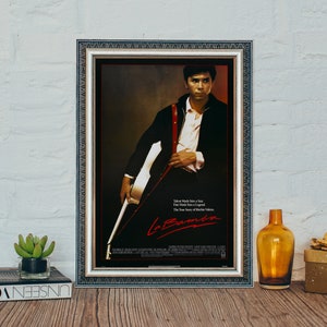 Könnte beinhalten: Ein gerahmtes Filmplakat für den Film "La Bamba" mit einem Schwarzweißfoto eines Mannes, der Gitarre spielt. Der Text auf dem Plakat lautet "Tale Made him a Star. Tale Made him a Legend. The True Story of Ritchie Valens. La Bamba."