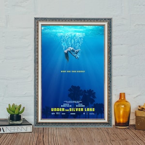 Könnte beinhalten: Gerahmtes Filmplakat für "Under the Silver Lake" mit einer blauen Unterwasserszene. Eine Figur taucht abwärts, mit dem Text "What Are They Hiding?" und dem Titel und den Credits des Films.