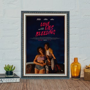 Peut inclure: Affiche encadrée du film "Love Lies Bleeding" avec Kristen Stewart. L'affiche présente un fond bleu foncé avec du texte rouge et deux personnes. L'affiche est dans un cadre argenté, exposée sur une surface en bois.