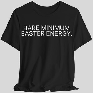 Puede incluir: Camiseta negra con el texto blanco "BARE MINIMUM EASTER ENERGY." La camiseta de manga corta está hecha de un material suave y es adecuada para ropa casual. El texto está centrado en la parte delantera de la camiseta.