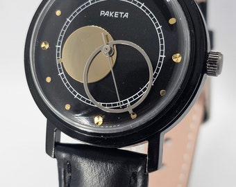 Puede incluir: Un reloj de pulsera negro con una correa de cuero negro. La esfera del reloj es negra con detalles dorados y presenta un diseño único de fase lunar. La esfera del reloj también tiene la palabra "PAKETA" impresa en ella.