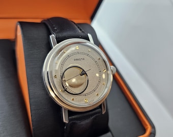 May include: A silver wristwatch with a black leather band. The watch face is white with gold accents and the word "PAKEТА" printed on it.