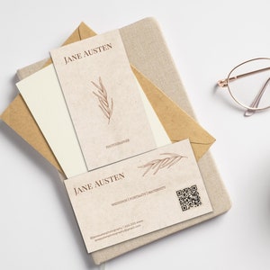 May include: Business cards with the name "Jane Austen" in a serif font, featuring a botanical illustration. The cards are beige with brown text and a QR code. The cards are on a beige notebook with a brown envelope.