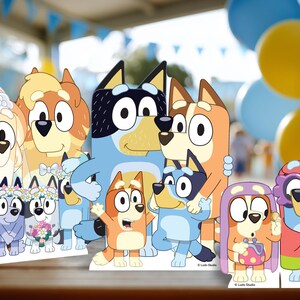 May include: A collection of colorful cardboard cutouts featuring cartoon dog characters. The characters are in various poses, some wearing flower crowns and holding bouquets. The background includes blue and yellow balloons, suggesting a party or celebration theme.