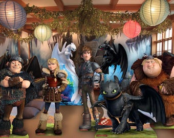 May include: A group of How to Train Your Dragon character cutouts, including Hiccup, Astrid, and Toothless, are displayed in a room decorated with paper lanterns and greenery. The characters are posed in front of a backdrop of a dragon-themed scene.