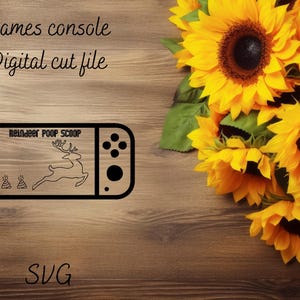 May include: Black and white digital cut file design of a video game console with the text "Reindeer Poop Scoop" and a cartoon reindeer on the screen. The design is on a woodgrain background with sunflowers.