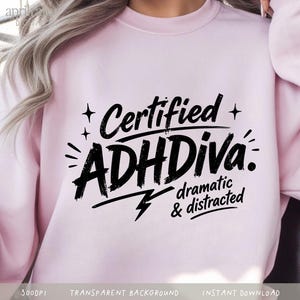 Può includere: Una felpa girocollo rosa chiaro con testo nero che recita Certified ADHDiva. dramatic & distracted. Il design include piccoli accenti a forma di stella e un fulmine. La felpa ha maniche lunghe e un colletto a coste.