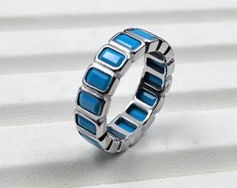 May include: A silver ring featuring a series of rectangular, turquoise-colored stones. The stones are set in a repeating pattern around the band, creating a continuous design. The ring is displayed on a white surface.