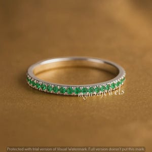 Puede incluir: Un anillo plateado con una banda de pequeñas gemas verdes vibrantes. El anillo está sobre un fondo dorado y cálido. El texto "myasajewels" es visible.