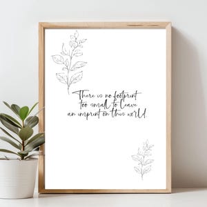 May include: A framed print with a light wood frame. The white background features black botanical line art and the quote, "There is no footprint too small to leave an imprint on this world." A potted plant is in the foreground.