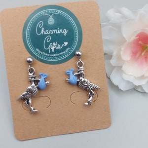 May include: A pair of silver earrings featuring a stork carrying a blue baby bundle. The earrings are on a brown card with the text "Charming Gifts" and a website address.