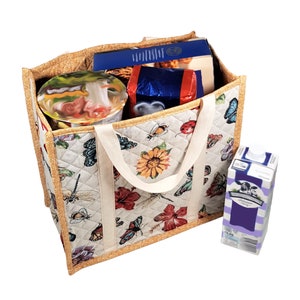 Puede incluir: Una bolsa de lona acolchada beige con un dise&ntilde;o floral y de mariposas. La bolsa tiene dos asas blancas y est&aacute; llena de varios art&iacute;culos, incluyendo una caja de cereales, un recipiente de fideos y una caja de leche.